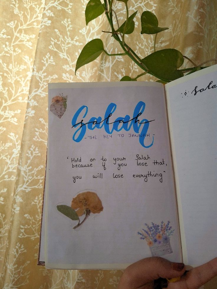 a person holding an open book with writing on it and a plant in the background