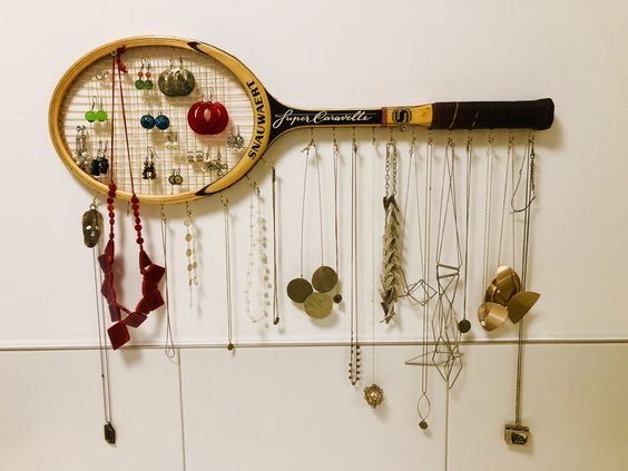 a tennis racket hanging on the wall with many necklaces and earring hooks