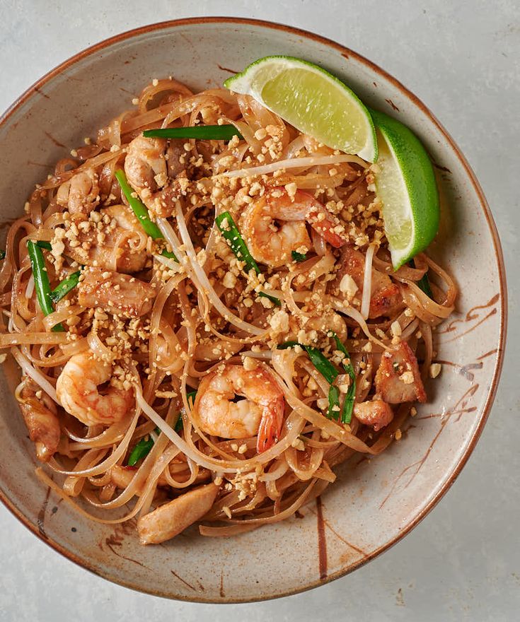 a white plate topped with noodles and shrimp next to a lime wedge on top of a table