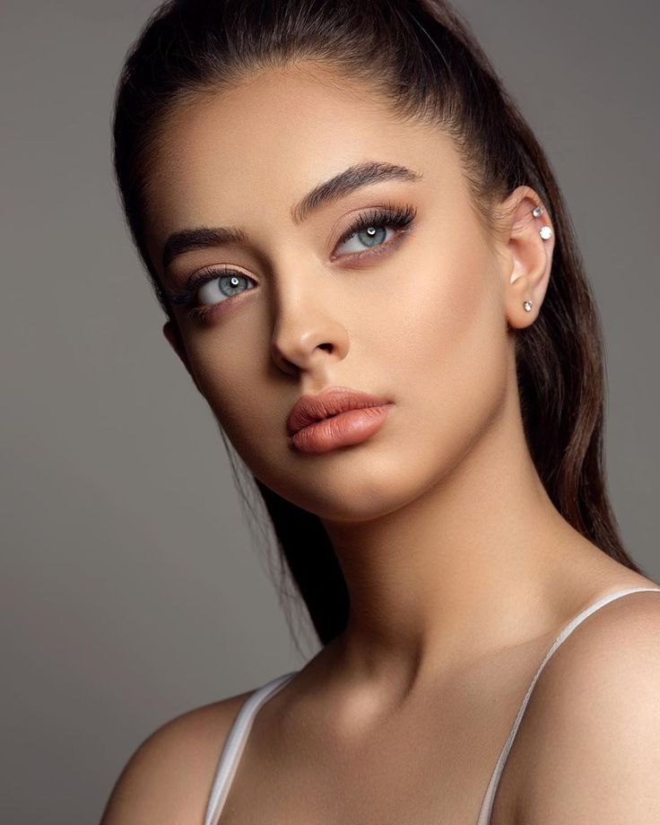 a woman with blue eyes and brown hair wearing a white bra top is looking at the camera