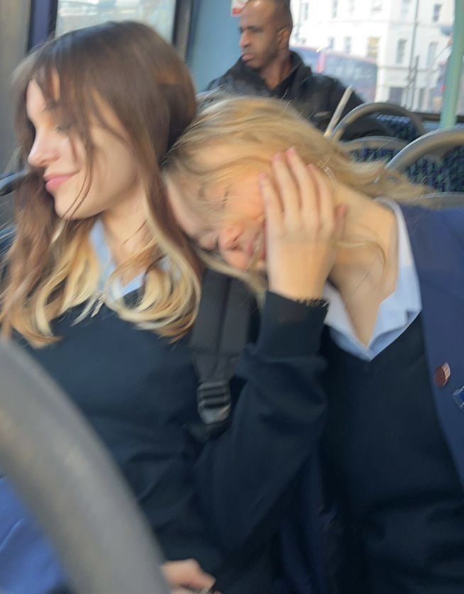 two women are sitting on a bus and one is holding her head