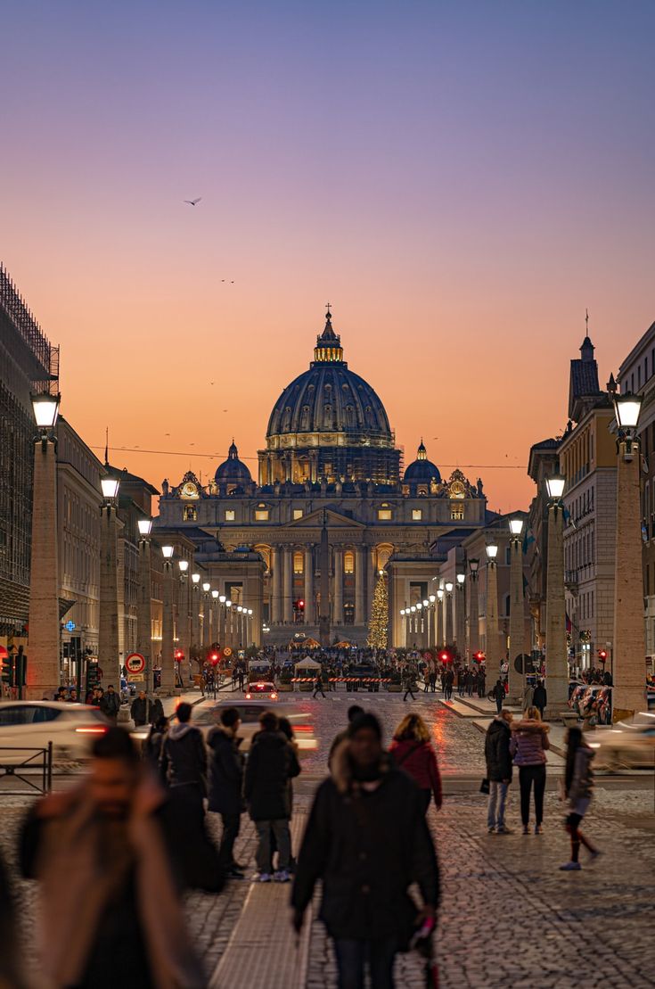 many people are walking down the street in front of some buildings at sunset or dawn