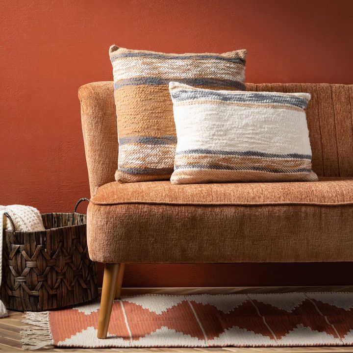 a couch with two pillows sitting on top of it next to a basket and rug