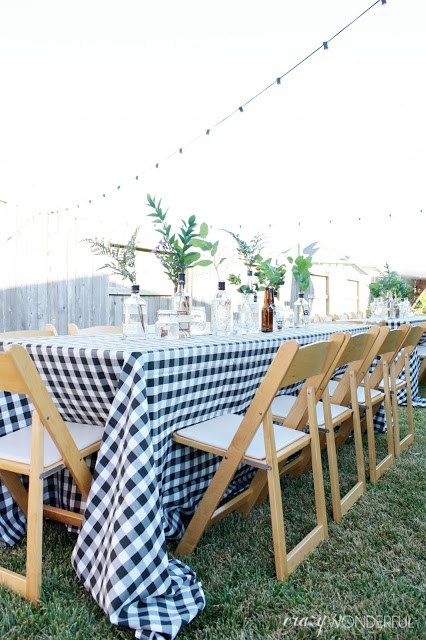 a long table with black and white checkered cloth on it is set up in the grass