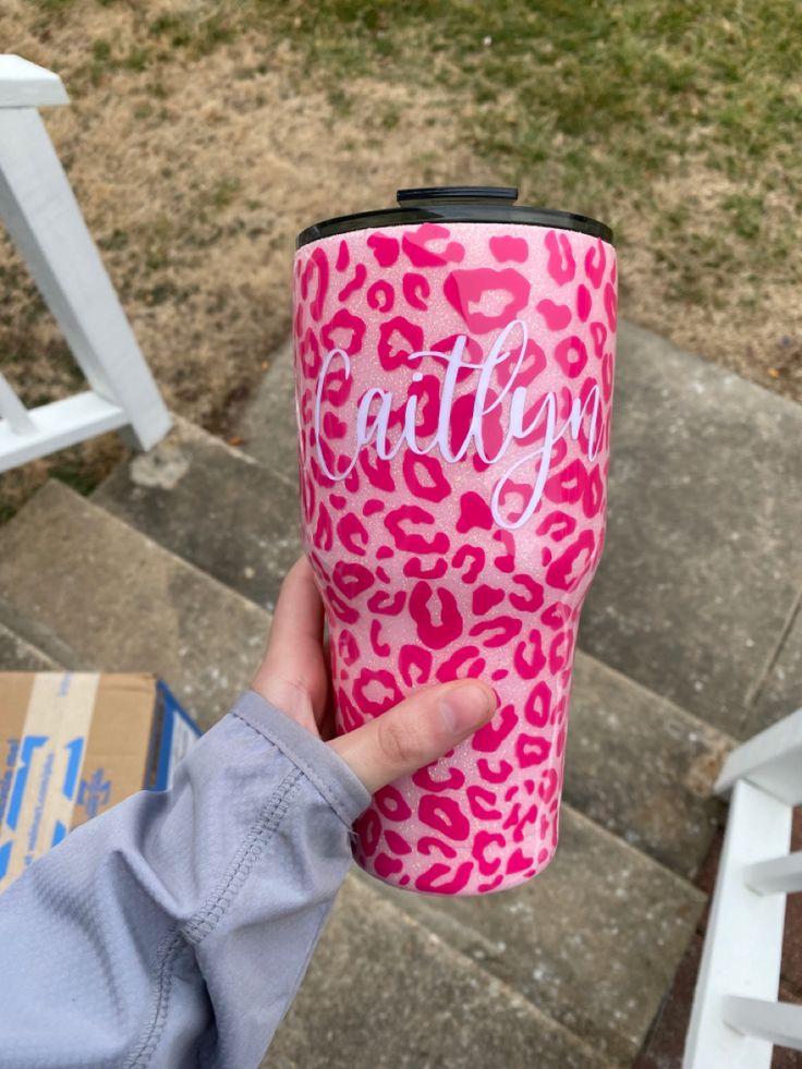 a person holding up a pink leopard print coffee cup with the word hello kitty on it