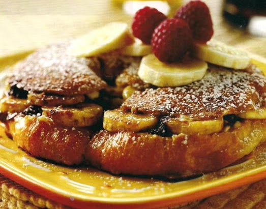 french toast with bananas, raspberries and powdered sugar on a yellow plate