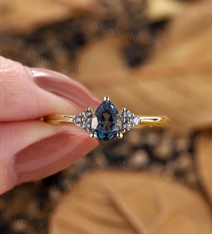 a woman's hand holding an engagement ring with two diamonds on the side and a blue diamond in the middle