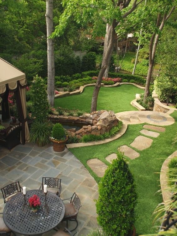 an outdoor patio area with tables and chairs, surrounded by lush green trees and shrubs