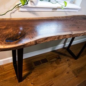 a wooden table with metal legs and a plant on it in front of a window