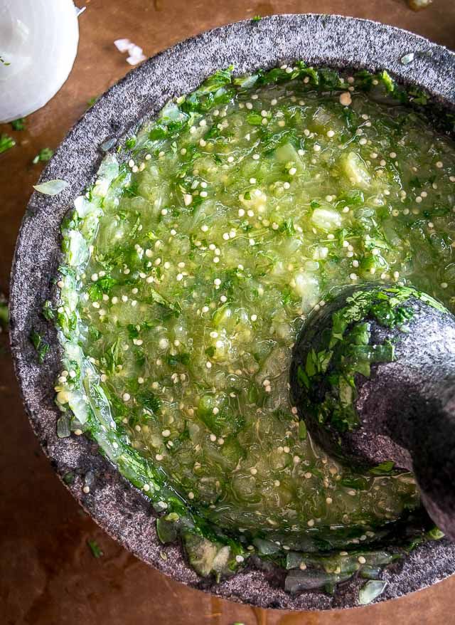 someone is dipping something into a bowl with green stuff in it on the table next to other ingredients