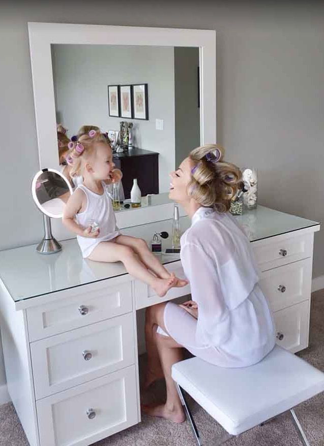 a woman sitting in front of a white desk with a mirror on top of it