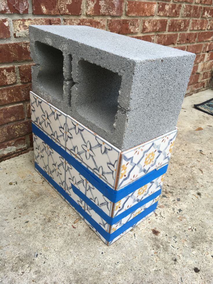 a cinder block sitting on top of a cement floor next to a brick wall with blue and white designs