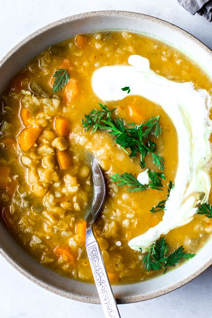 a bowl of soup with carrots, beans and sour cream in it next to a spoon