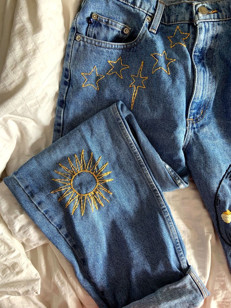 two pairs of jeans with embroidered sun and stars on them, sitting on a bed