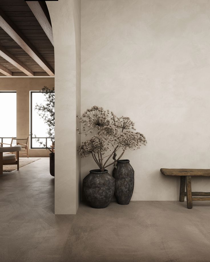 two vases with flowers are sitting on the floor next to a bench in an empty room