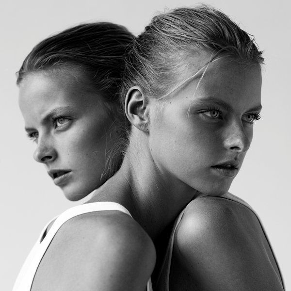 two beautiful women standing next to each other in front of a white background with one woman looking at the camera