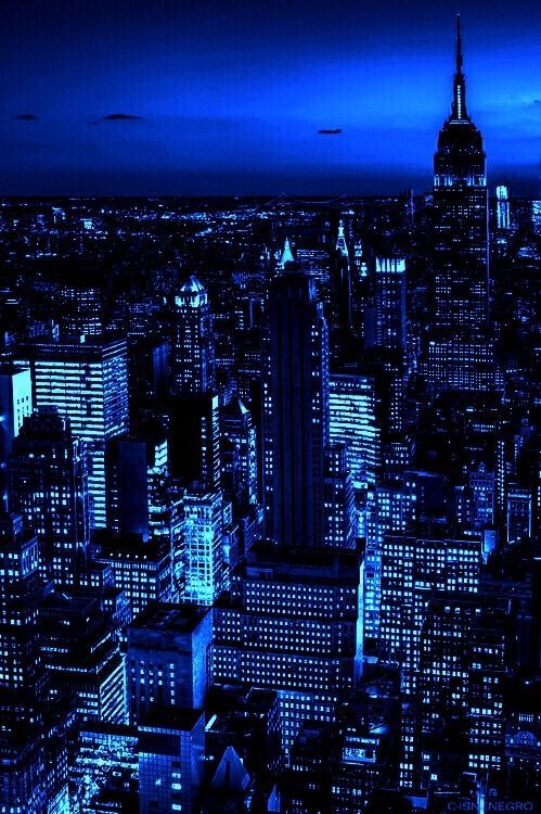 an aerial view of new york city at night with the empire building lit up in blue