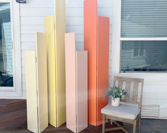 four tall, multicolored panels sitting on top of a wooden floor next to a chair