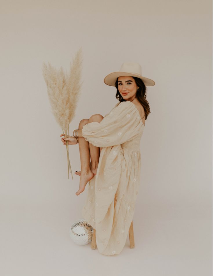 a woman in a white dress and hat holding a tall plant next to an egg