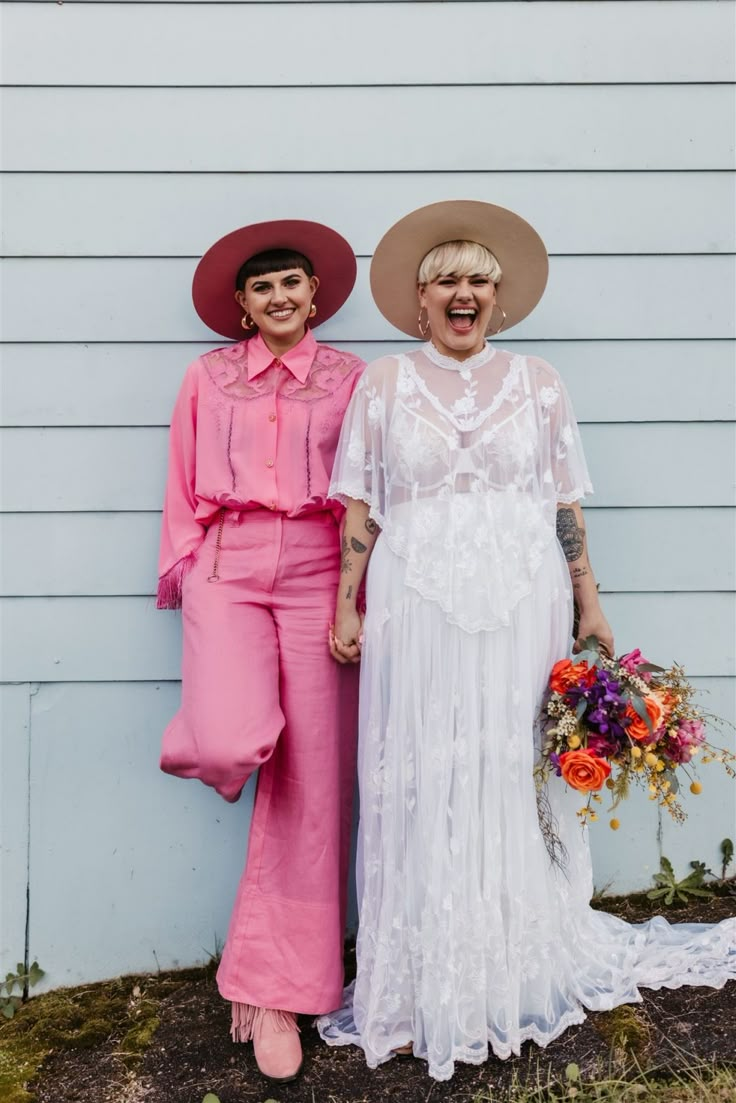 two women standing next to each other in front of a white wall wearing hats and dresses