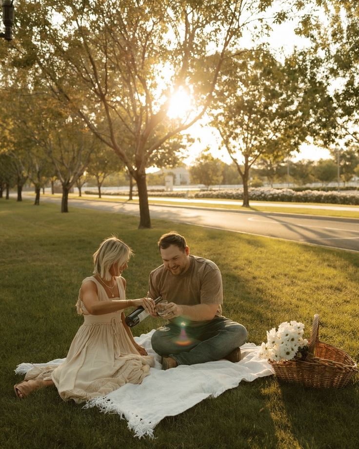 a man kneeling down next to a woman on top of a blanket in the grass