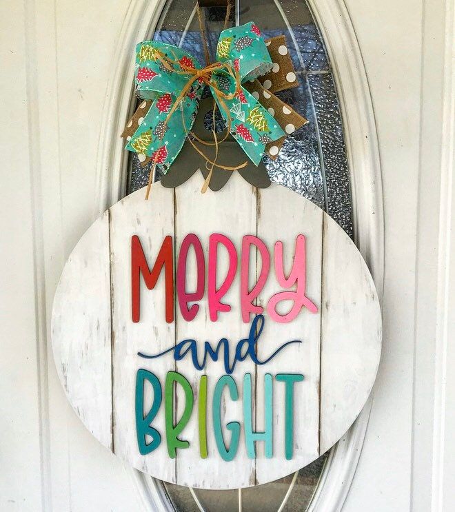 a merry and bright door hanger on the side of a white door with a bow