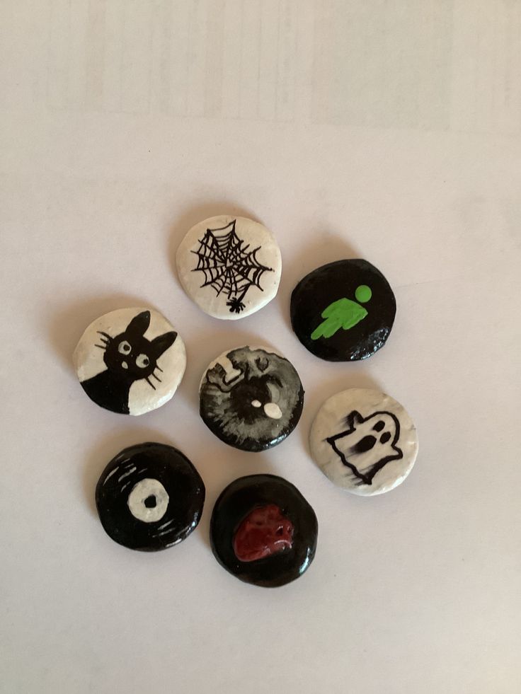 six buttons with black and white designs are arranged on a table, one has a green spider