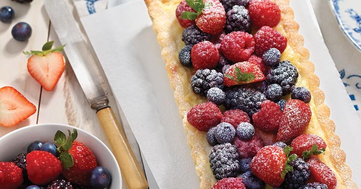 a pastry with berries and powdered sugar on it next to a bowl of strawberries