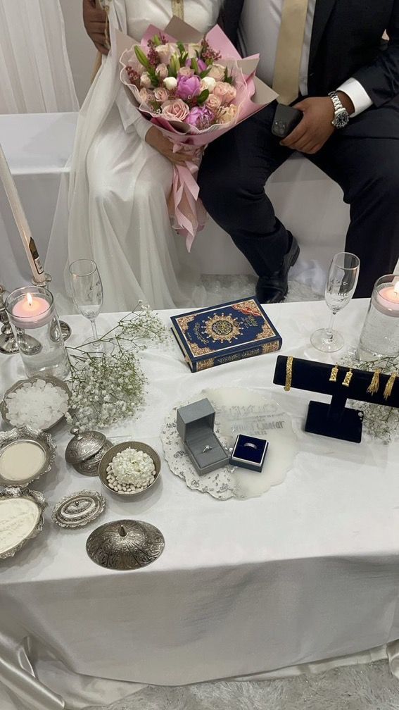 a bride and groom sitting at a table with flowers, candles, and other items on it