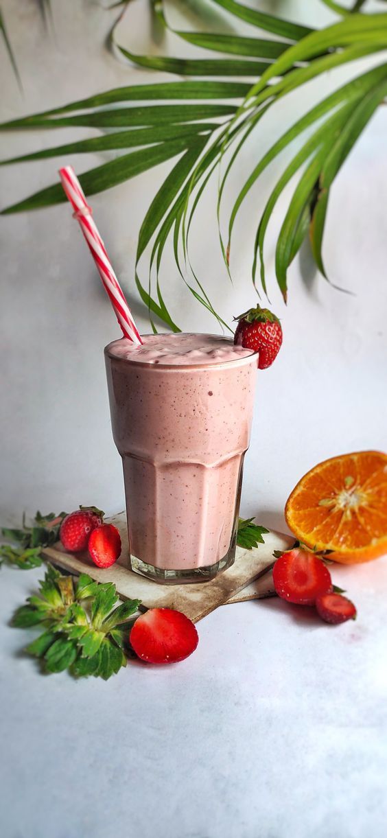 a smoothie is garnished with strawberries, oranges and palm leaves