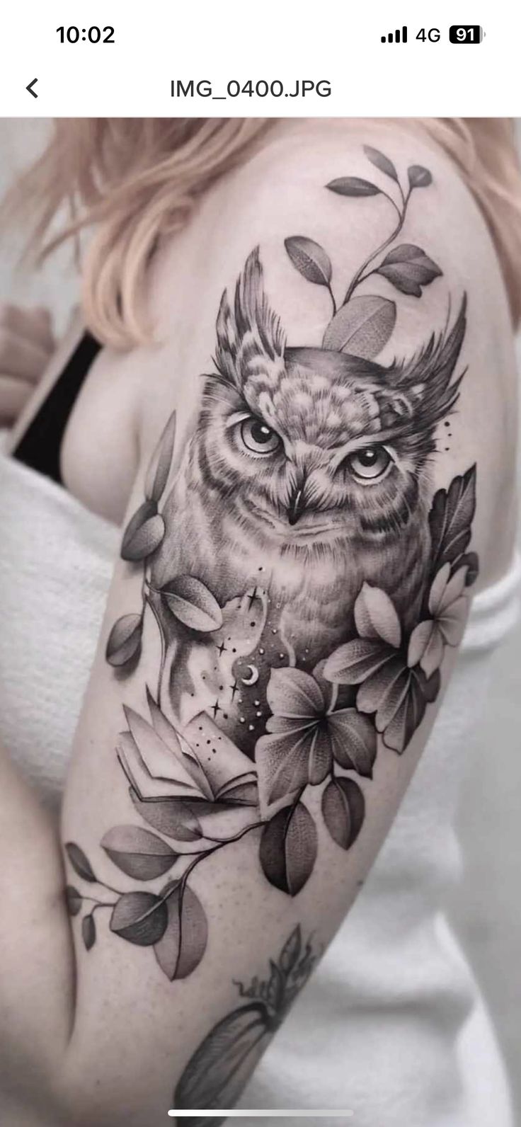 an owl and flowers tattoo on the right arm, with leaves around its neck in black and white