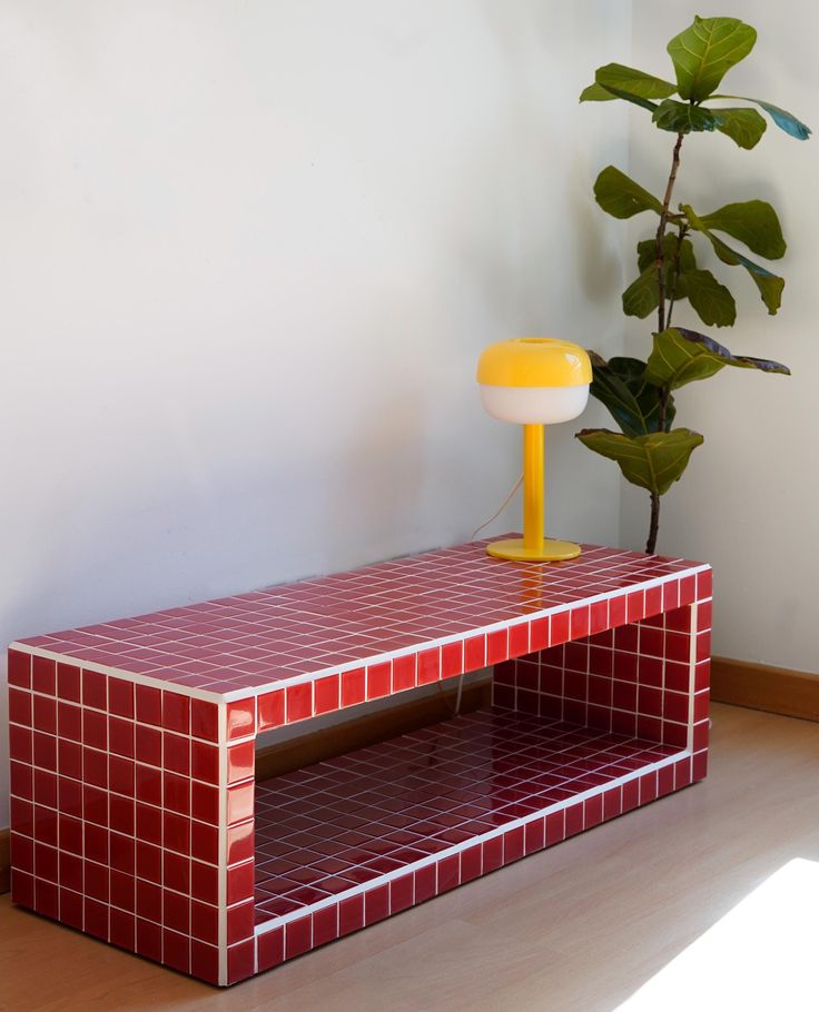 a red table with a yellow lamp on top and a potted plant in the corner