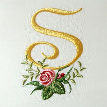 the letter s is decorated with flowers and gold thread on a white background, it appears to be embroidered onto fabric