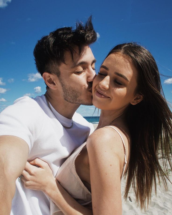 a man and woman kissing on the beach with blue skies in the backgroud