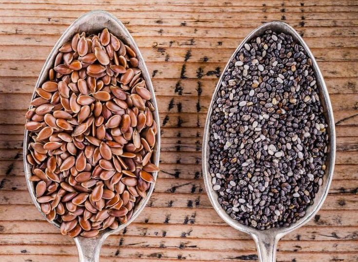 two spoons filled with seeds on top of a wooden table