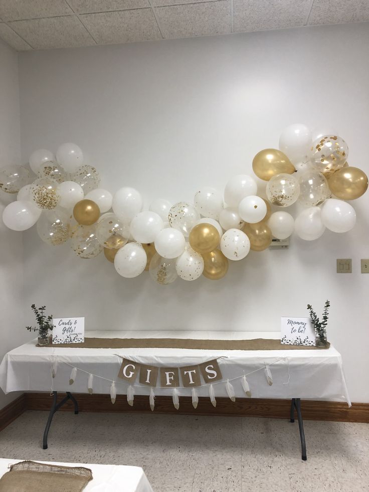 a table with white and gold balloons hanging from it's sides in front of a wall