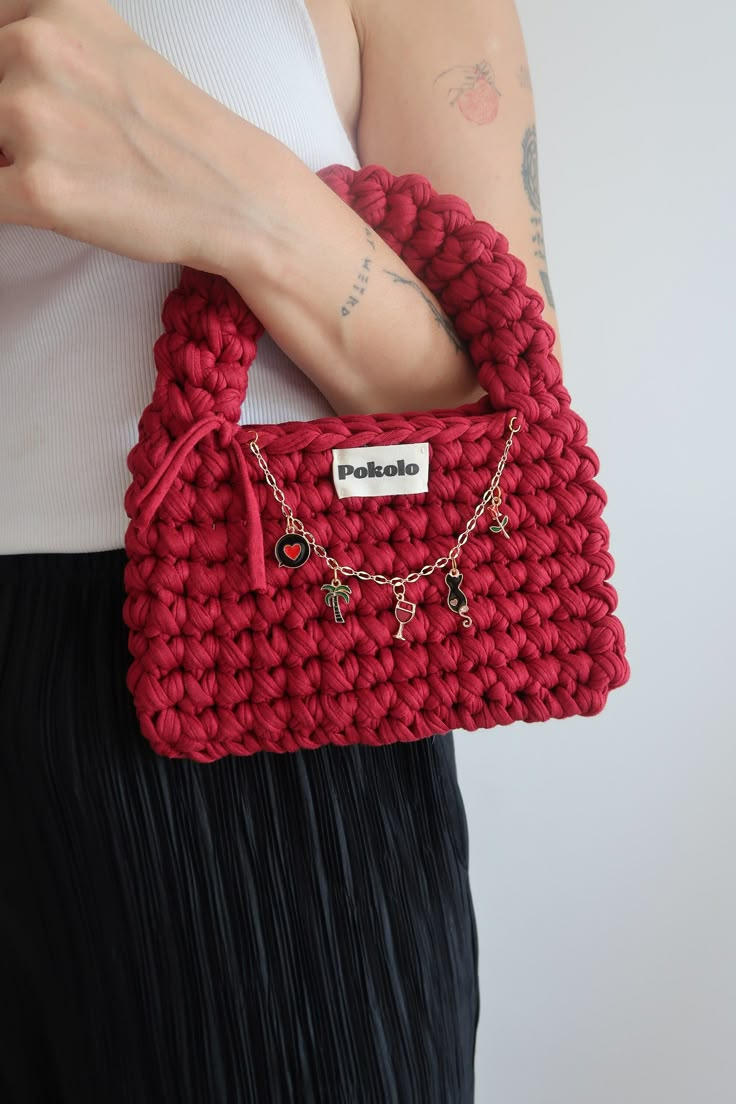 a woman holding a red crocheted purse with chains attached to the front pocket