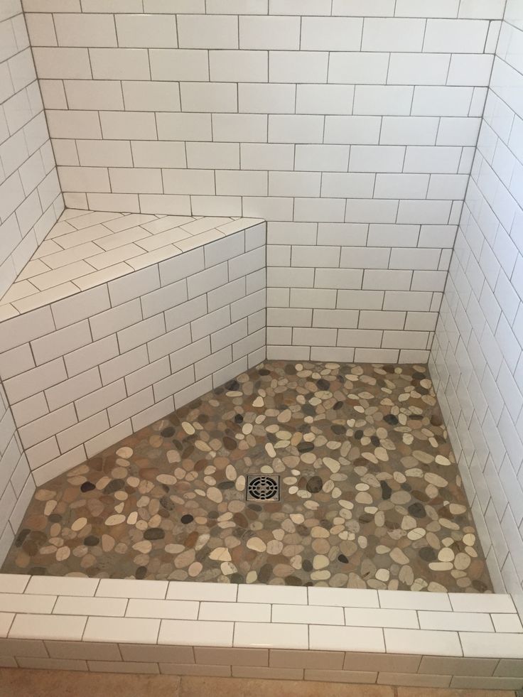 a white tiled shower stall with pebbles on the floor