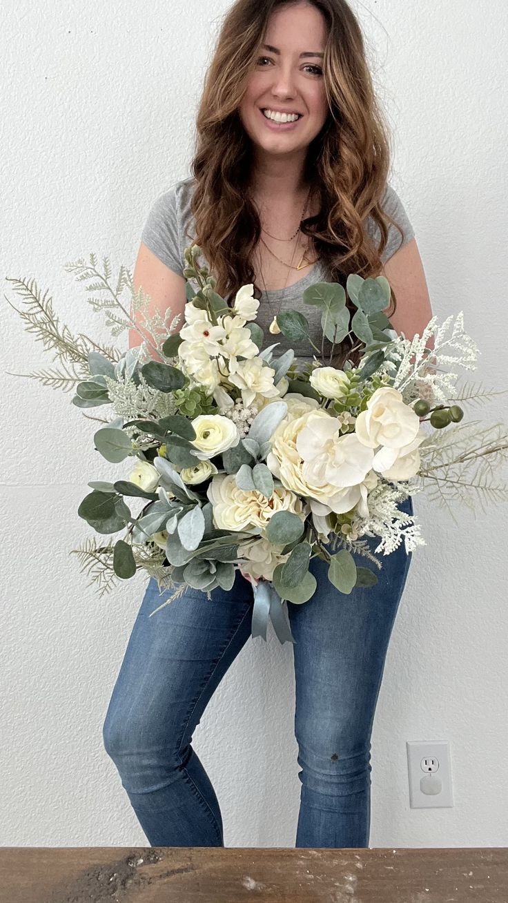 a woman holding a bouquet of flowers on top of a wooden table in front of a white wall