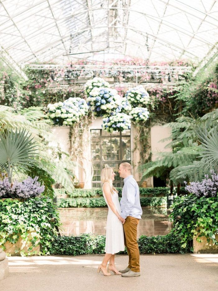 an engaged couple standing in the middle of a greenhouse surrounded by flowers and greenery