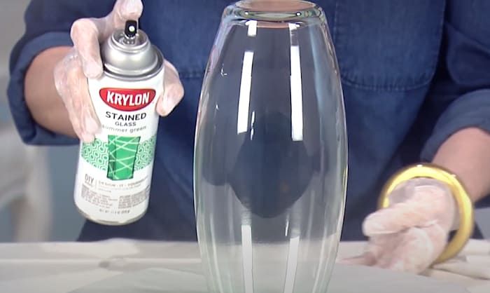 a person in blue shirt and white gloves holding a spray bottle next to a glass vase