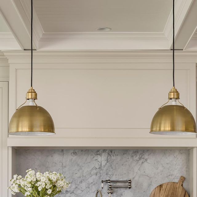 a kitchen with marble counter tops and gold pendant lights over the sink, next to a wooden cutting board