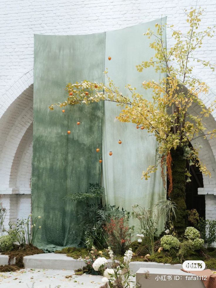 an outdoor area with various plants and flowers on the ground next to a large green curtain