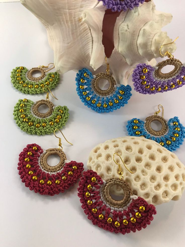 several different types of beaded earrings are displayed on a white table next to shells and seashells