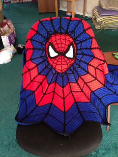 a crocheted spiderman chair sits in the middle of a room with green carpet