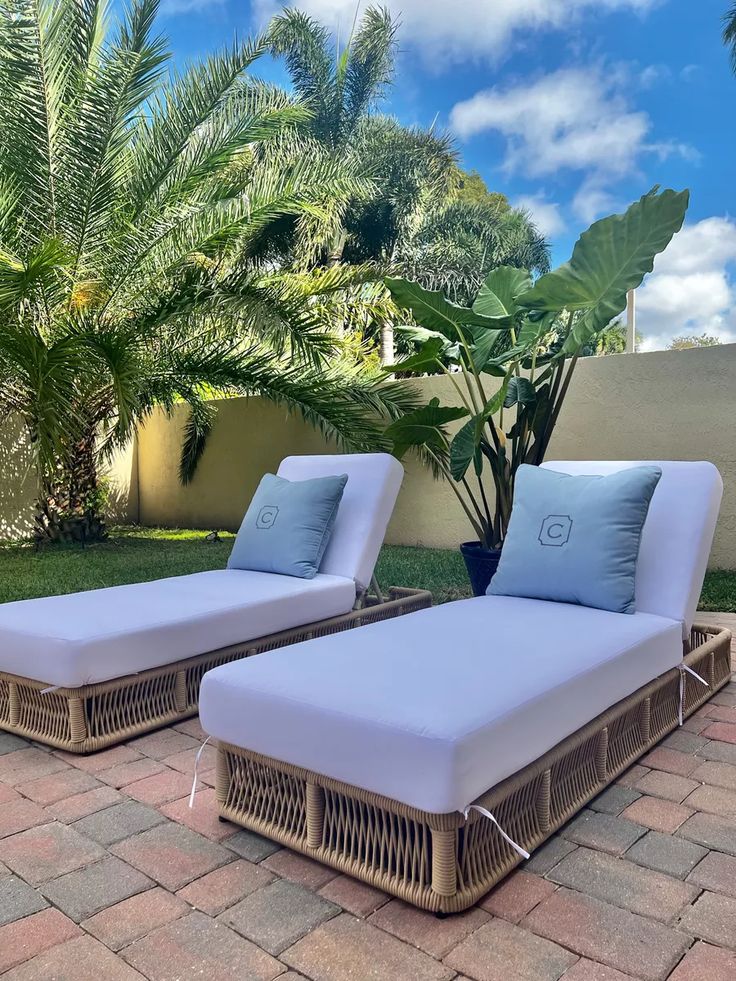 two wicker chaise lounges with blue cushions in front of a palm tree