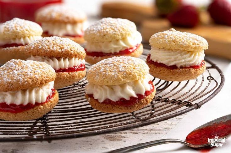 small pastries are sitting on a wire rack with strawberries in the back ground