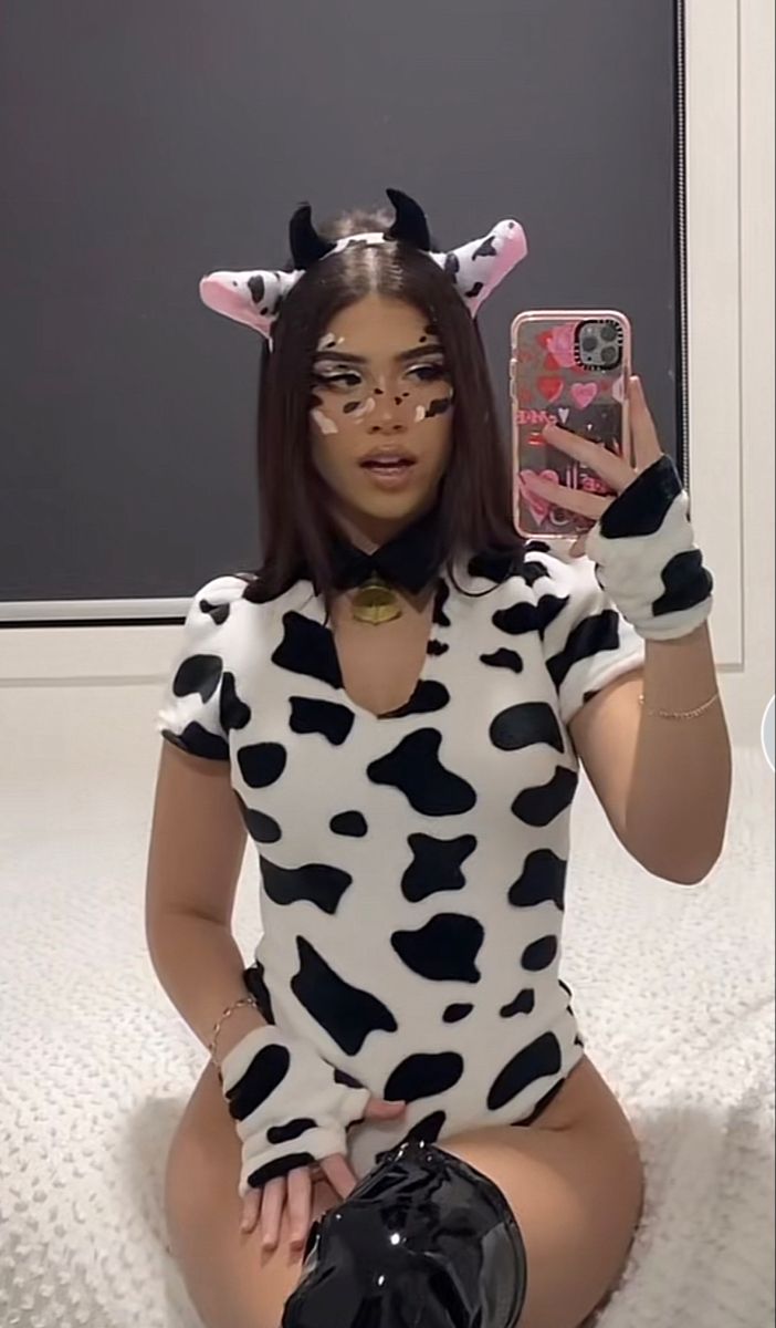 a woman in a cow costume is taking a selfie with her cell phone while sitting on the floor