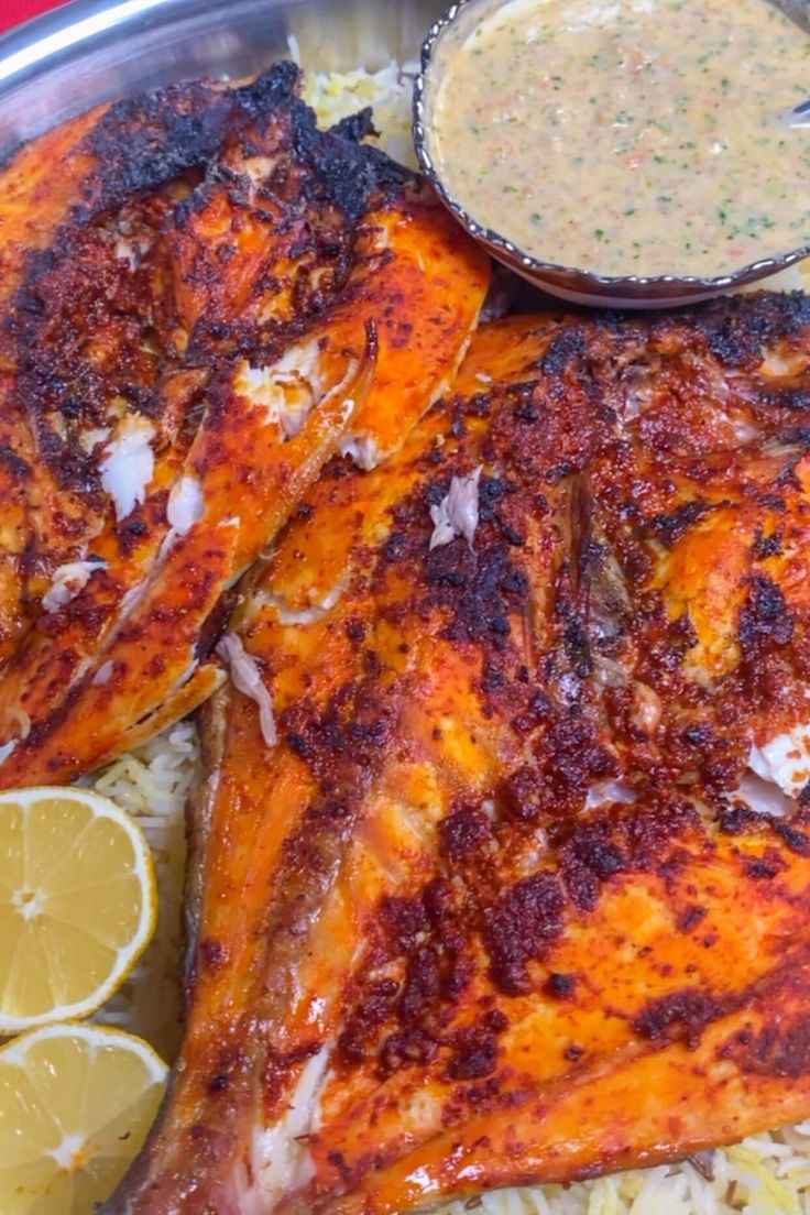 two pieces of fish on top of rice and lemon wedges next to dipping sauce