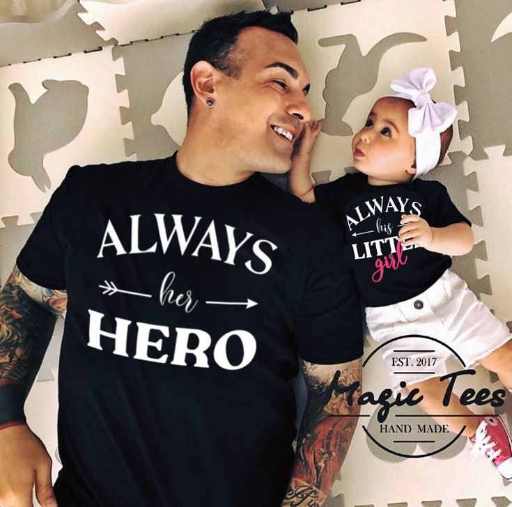 a man holding a baby while wearing a t - shirt that says always her hero